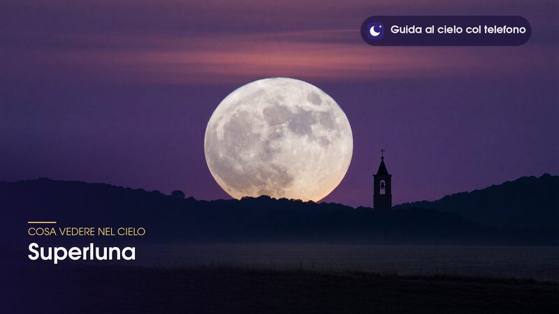 Superluna bassa sull'orizzonte, ripresa con il teleobiettivo dietro colline e un campanile